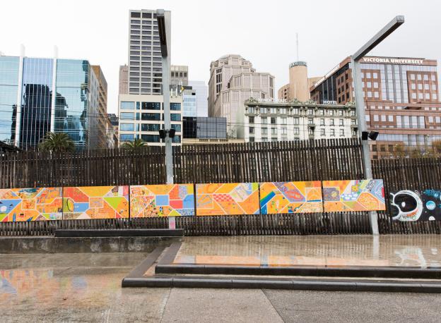 A painted mural is on top of a wooden fence overlooking the Melbourne city skyline